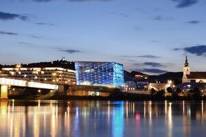 Aufnahme des Ars Electronica Centers in Linz bei Nacht inklusive Spiegelung im Flusswasser.